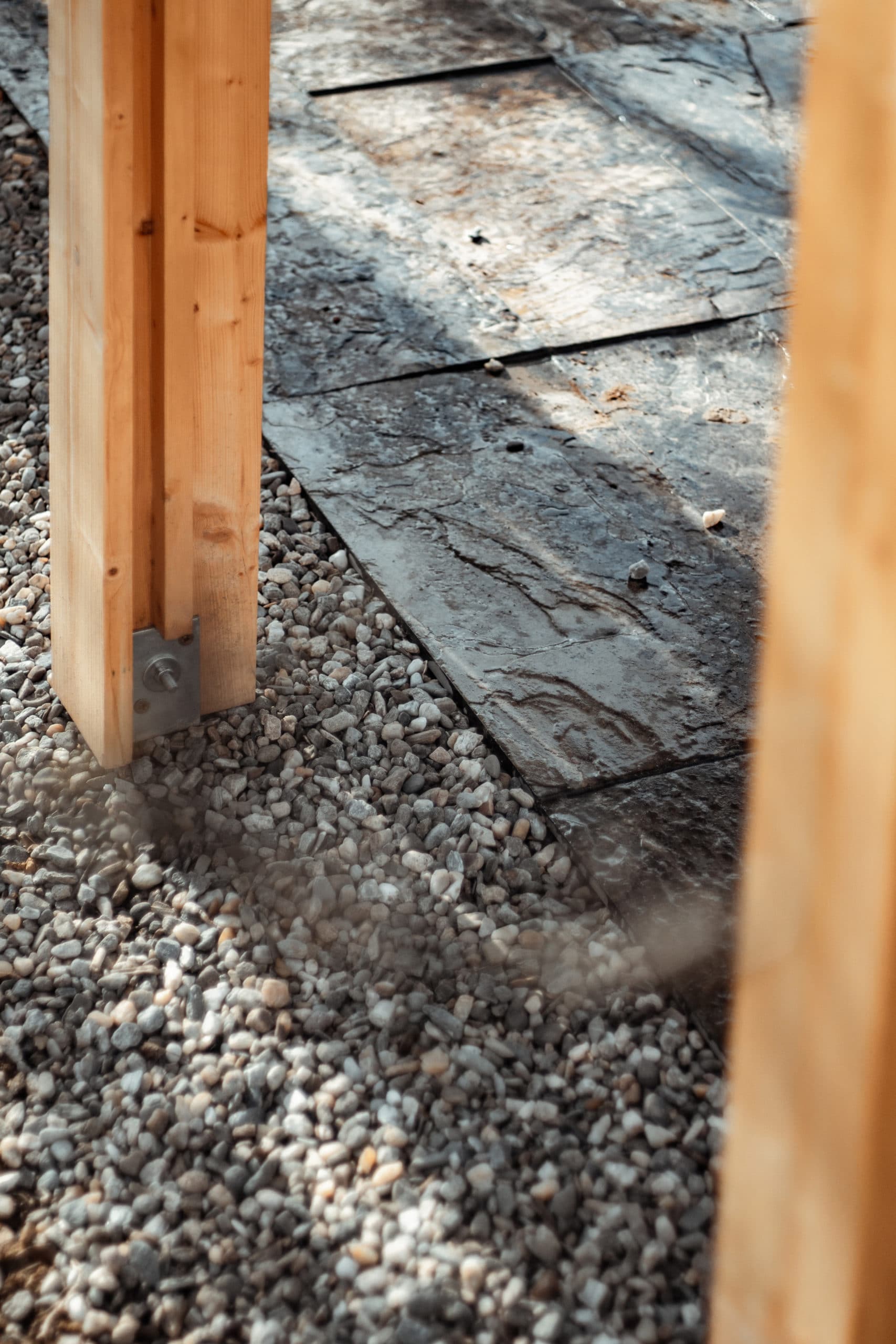 T section wood pillars we built ourselves, held by metal post bases right over gravel area.