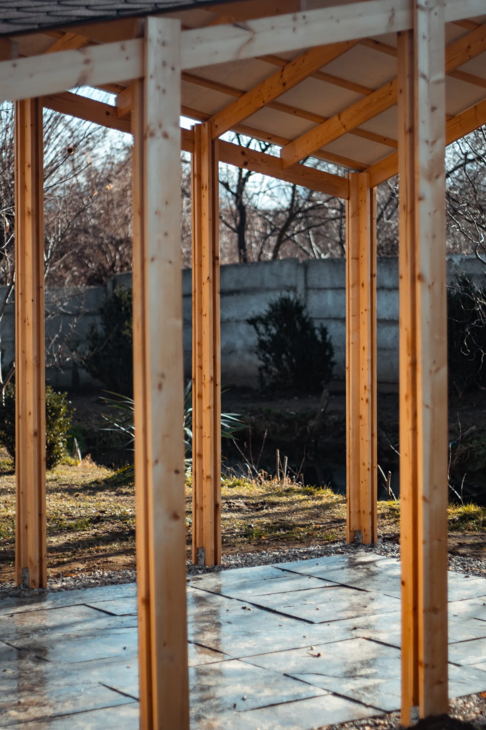 The beam made out of a wood plank goes through the evergreen wood posts.